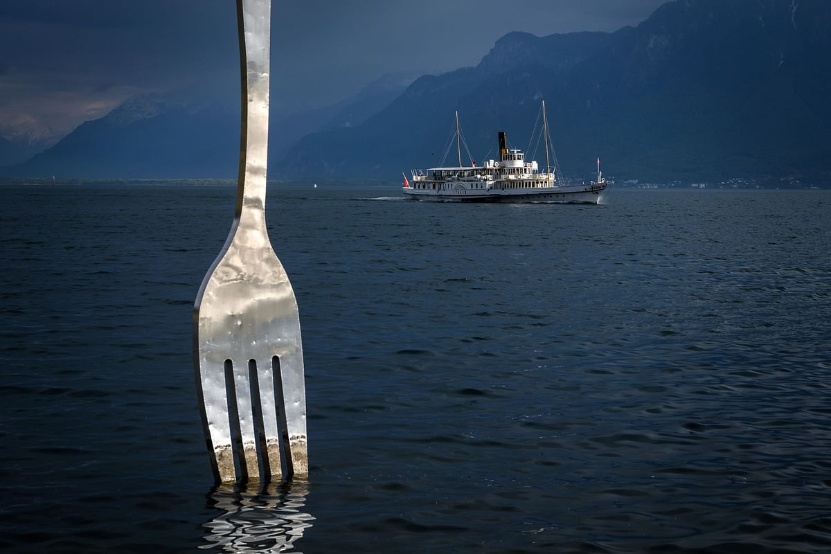 A picture taken on 21 May 2019 in Vevey shows the paddle steamer `Italie` of the Compagnie Generale de Navigation sur le lac Leman, commonly abbreviated to CGN, sailing on Lake Geneva past a giant fork sculpture designed by Switzerland`s artist Jean-Pierre Zaugg. Vevey, Canton of Vaud, Switzerland. Photo: AFP