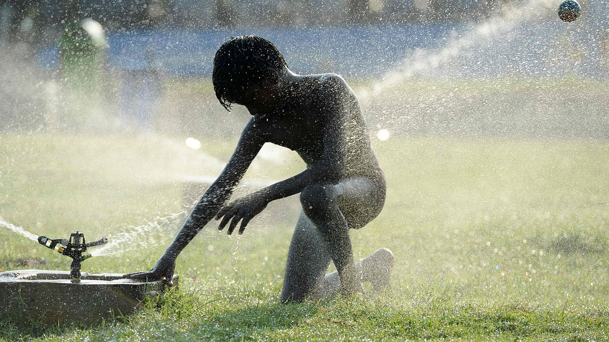An Indian boy plays with water sprinklers at Marina Beach during a hot day in Chennai on 27 May 2019. Photo: AFP