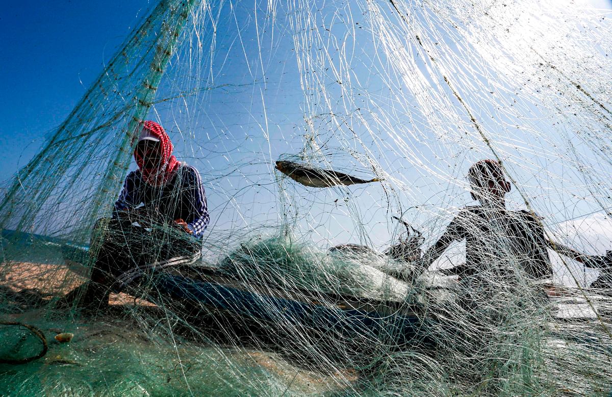 Palestinian fishermen sit in a beached fishing boat as they mend a fishing net along the coast in Khan Yunis in the southern Gaza Strip on 14 June, 2019. Photo: AFP