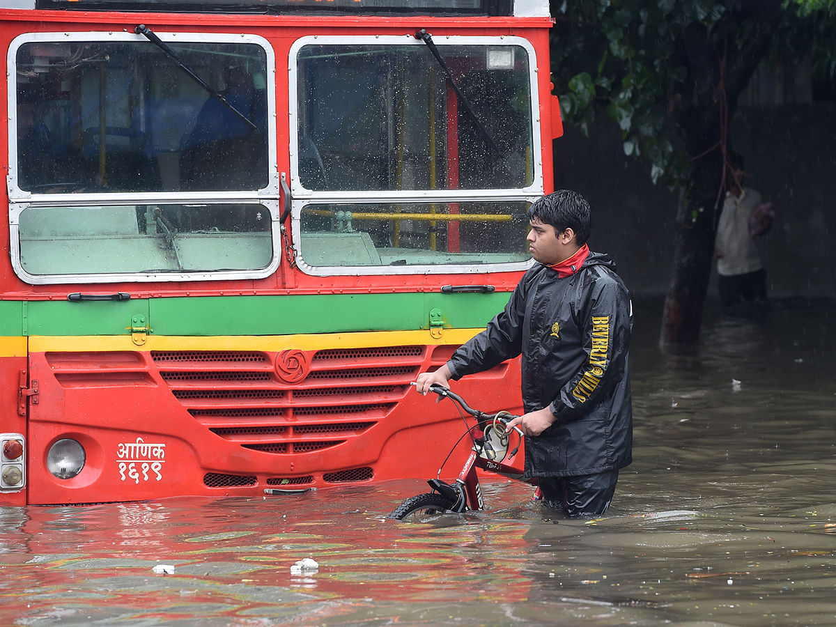An Indian man wheels a bicycle along a flooded street after heavy rain showers in Mumbai on 1 July. Photo: AFP