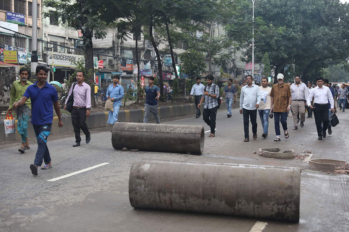 People walk past barriers placed on the road allegedly by protesters during a hartal against the recent gas price hike. Paltan, Dhaka on 7 July 2019. Photo: Saiful Islam