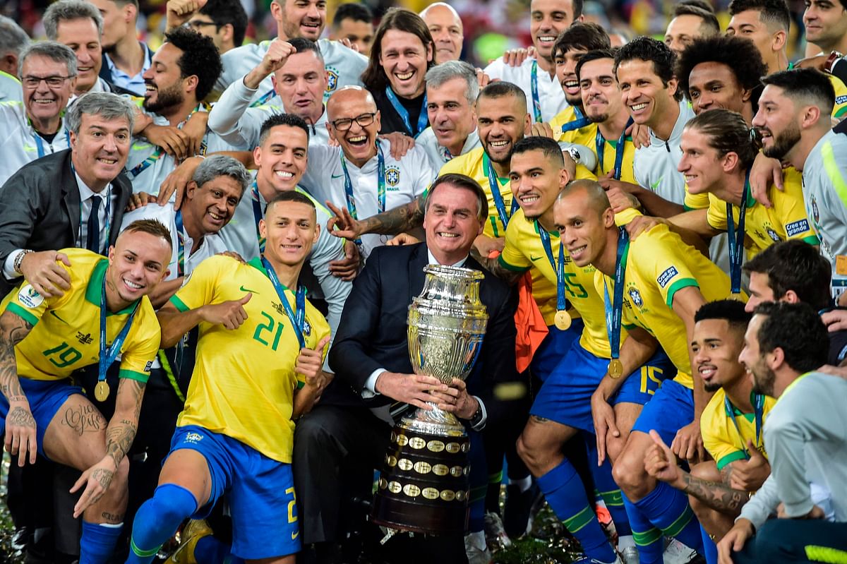 Brazilian president Jair Bolsonaro holds the Copa America trophy as members of the Brazilian national team celebrates after winning the title by defeating Peru in the final match of the football tournament at Maracana Stadium in Rio de Janeiro, Brazil, on 7 July, 2019. Photo: AFP