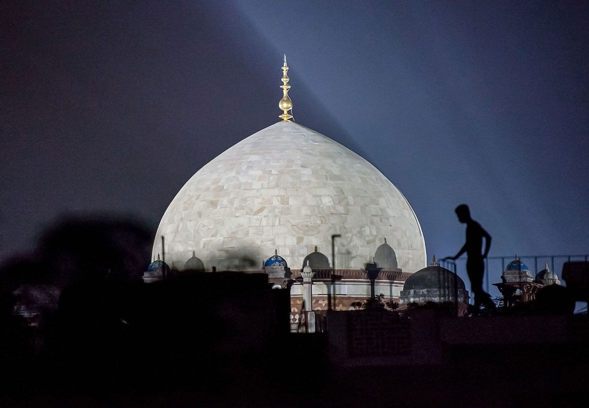 In this photo taken on 7 July 2019 a man stands on a roof near the illuminated dome of Humayun`s Tomb, a 16th century Mughal monument, in the Indian capital New Delhi. Photo: AFP