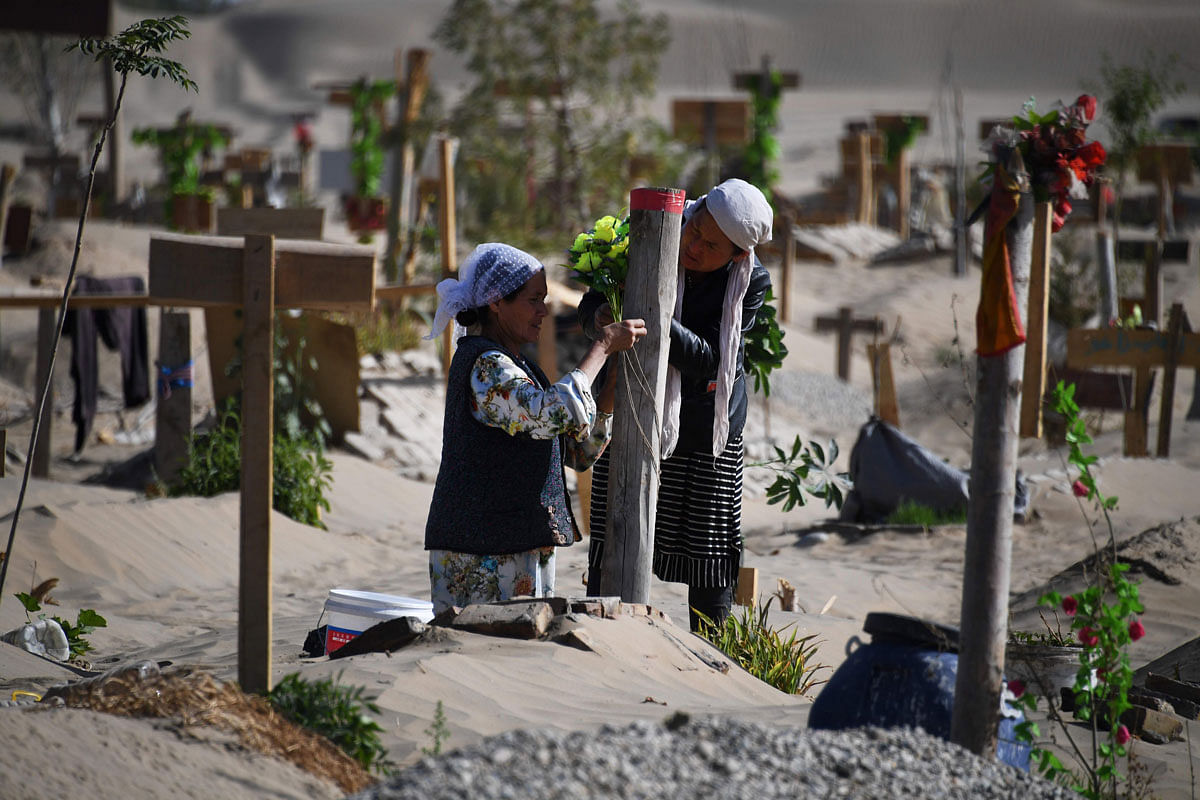 This photo taken on 31 May 2019 shows two women decorating a grave in a Uighur graveyard on the outskirts of Hotan in China`s northwest Xinjiang region. China has enforced a massive security crackdown in Xinjiang, where more than one million ethnic Uighurs and other mostly Muslim minorities are believed to be held in a network of internment camps that Beijing describes as `vocational education centres` aimed at steering people away from religious extremism. Photo: AFP