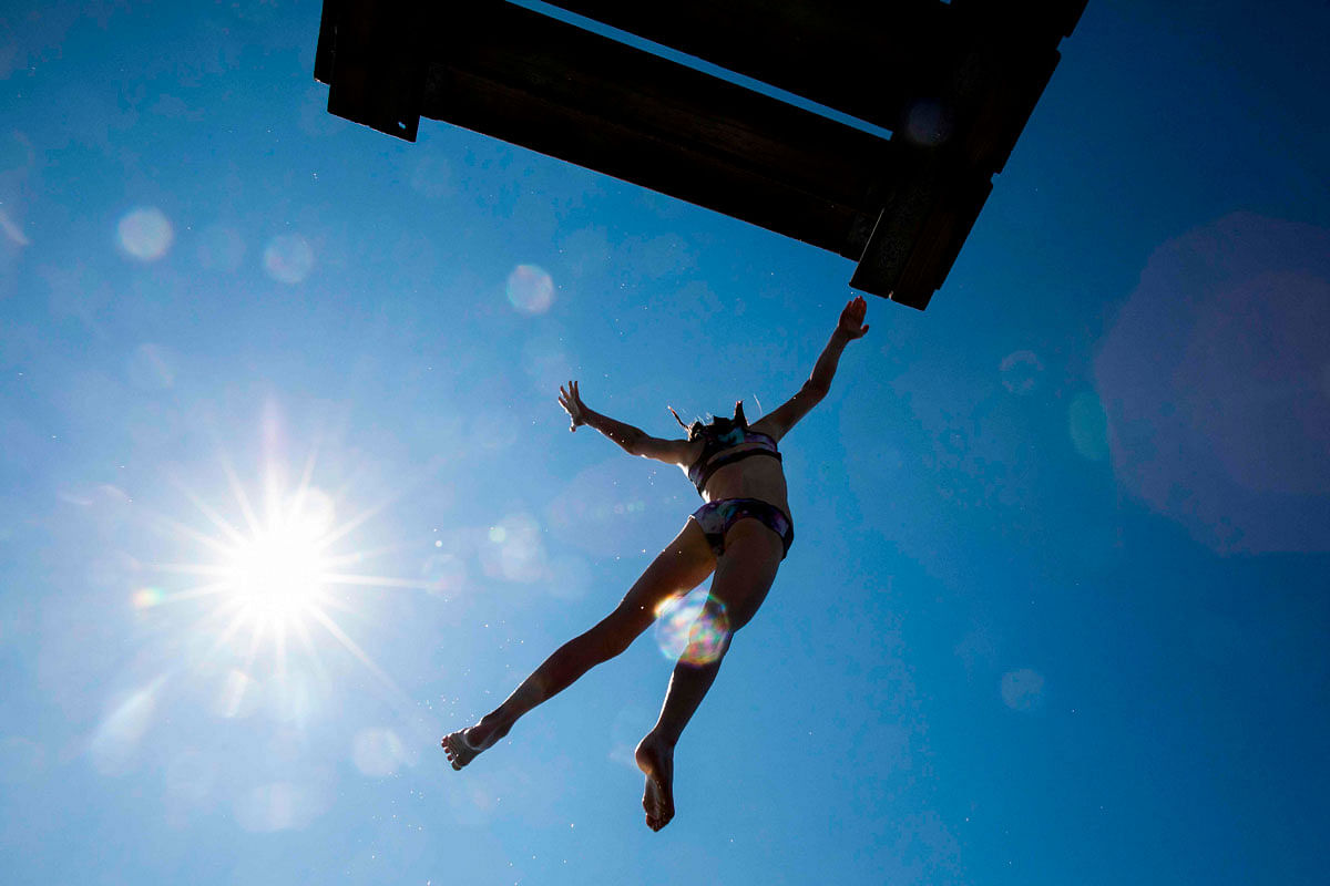 A  girl is silhouetted against the sun as she jumps into the sea from a diving board on Lindoya island in Oslo on 10 July 2019. Forecasts predicts 27 celsius in the Norwegian capital on Wednesday and the water temprature is expected to reach 18. Photo: AFP