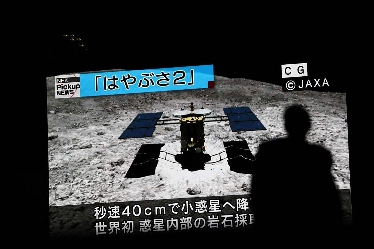 In this picture taken on 10 July 2019 a man walks past a screen displaying a computer-generated image of the Hayabusa2 probe, during a news broadcast at Akihabara district in Tokyo. Japan`s Hayabusa2 probe landed successfully on a distant asteroid for a final touchdown on 11 July 2019, hoping to collect samples that could shed light on the evolution of the solar system. Photo: AFP