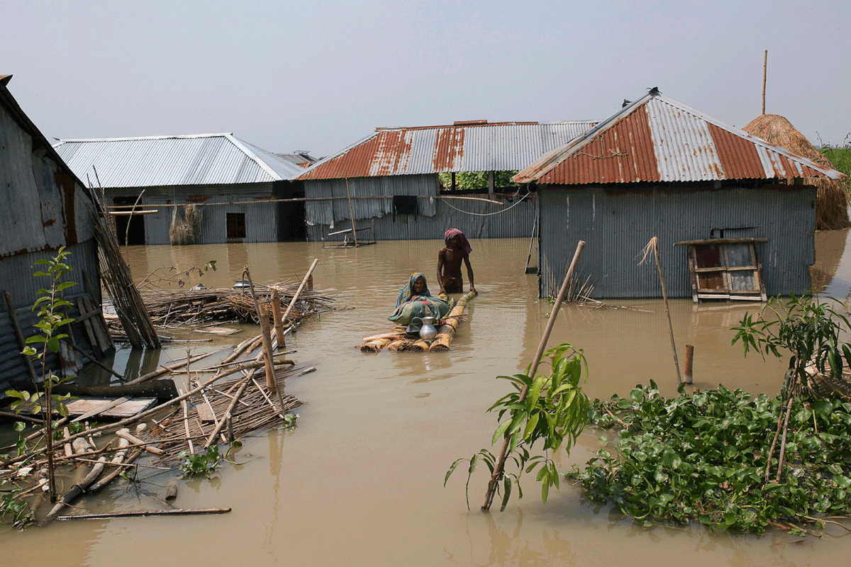 People walk in floodwaters as they transport belongings on a makeshift raft following heavy monsoon rains at a flood affected area of Gaibandha district, in Northern Bangladesh, on 19 July, 2019. Photo: AFP