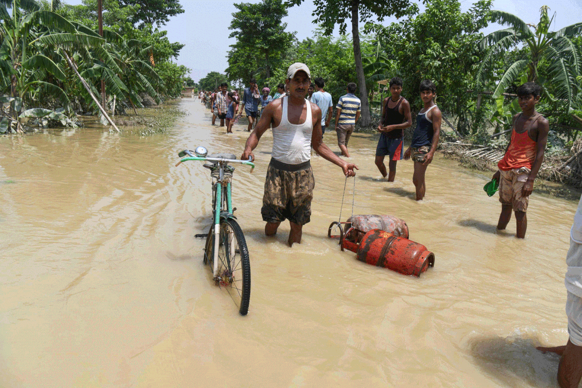 An Indian resident wades on a flooded road leading his bicycle and carrying gas bottles following heavy monsoon rains at Muzaffarpur district in the Indian state of Bihar on 18 July, 2019. Photo: AFP