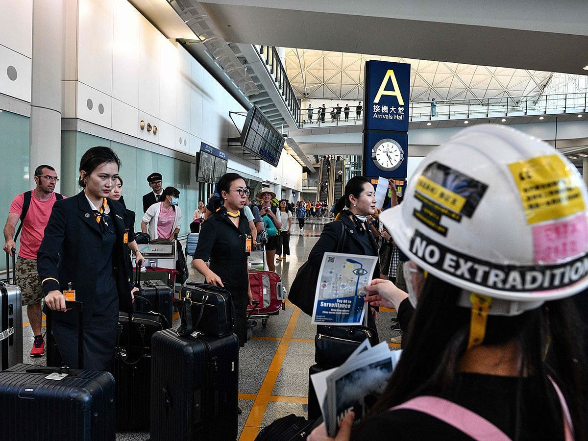 Cabin crew walk past a protester handing out leaflets and chanting slogans as protesters rally against a controversial extradition bill in the arrivals hall of the international airport in Hong Kong on 26 July 2019. Photo: AFP