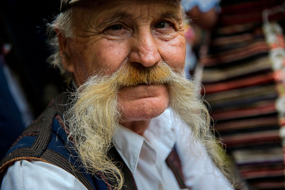 A participant in the longest moustache competition poses outside the 15th century Kalenic Serbian Orthodox monastery, near Rekovac, central Serbia on 4 August 2019. Photo: AFP
