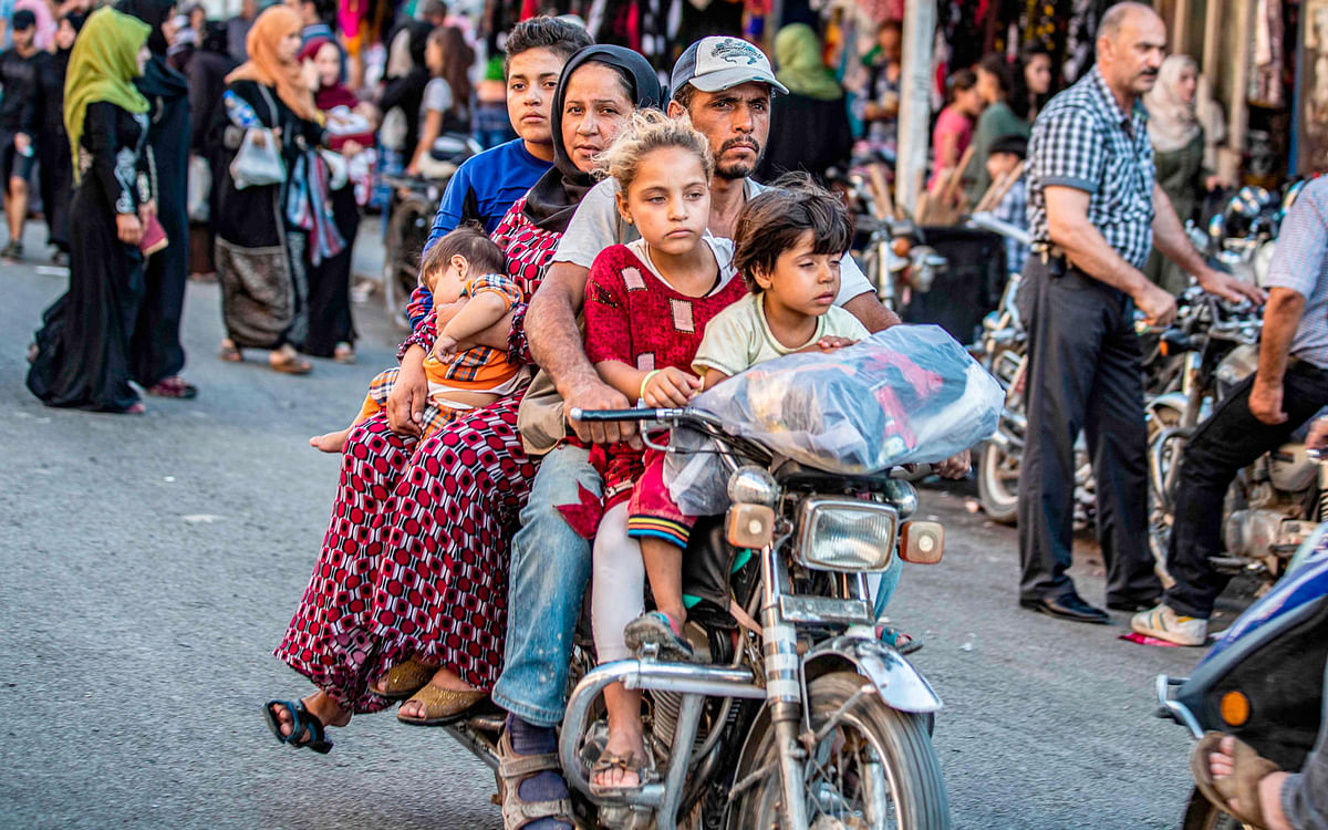 A man rides a motorcycle with a woman and children through a street market in the predominantly-Kurdish northeastern Syrian city of Qamishli on 5 August 2019. Photo: AFP