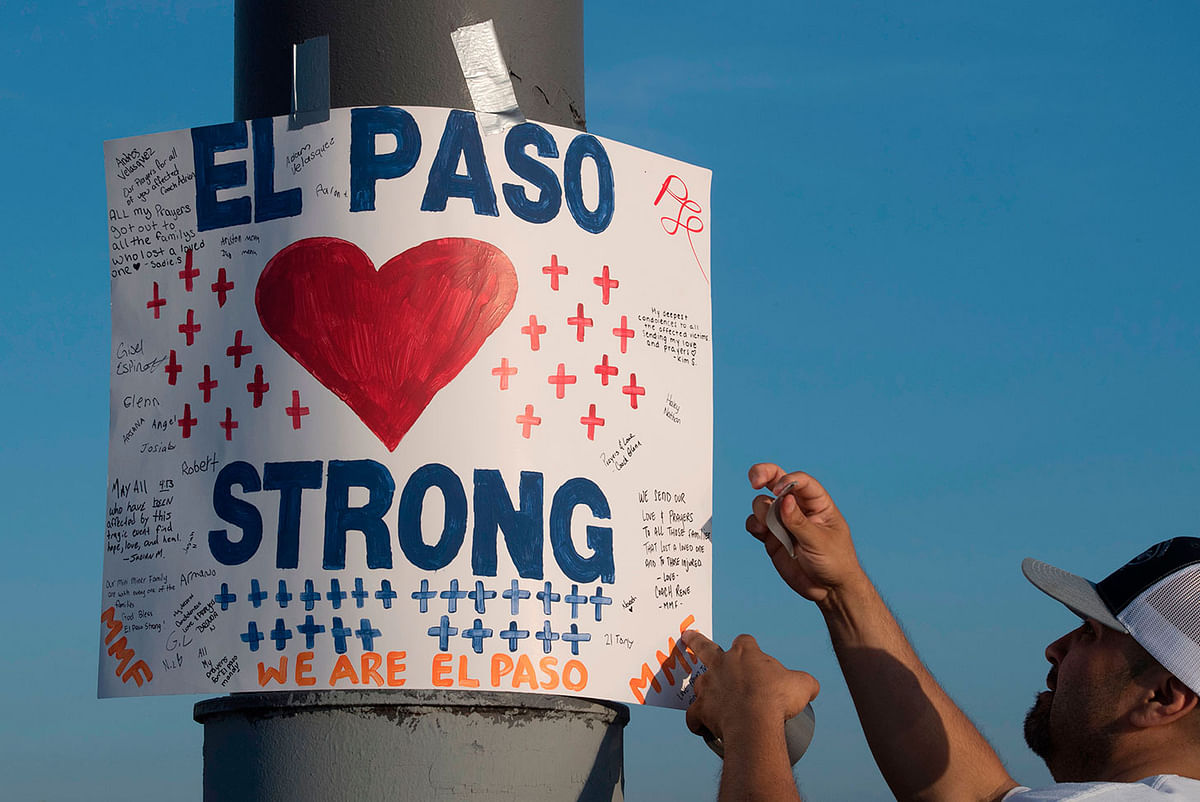 Coach Rene installs a `El Paso Strong` sign at the makeshift memorial for victims of the shooting that left a total of 22 people dead at the Cielo Vista Mall WalMart (background) in El Paso, Texas, on 6 August 2019. Photo: AFP