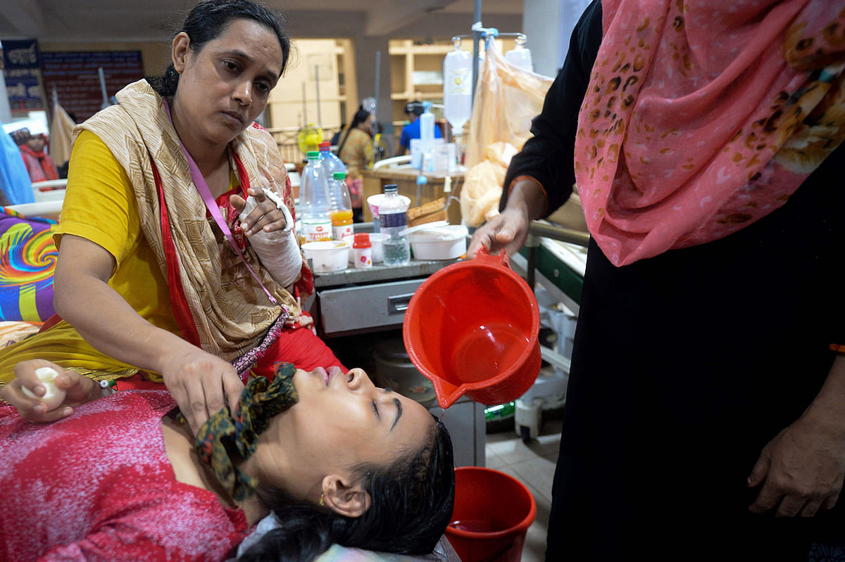 A Bangladeshi woman pours water on a dengue patient`s forehead to cool her fever, at the Mugda Medical College and Hospital in Dhaka on 8 August, 2019. Photo: AFP