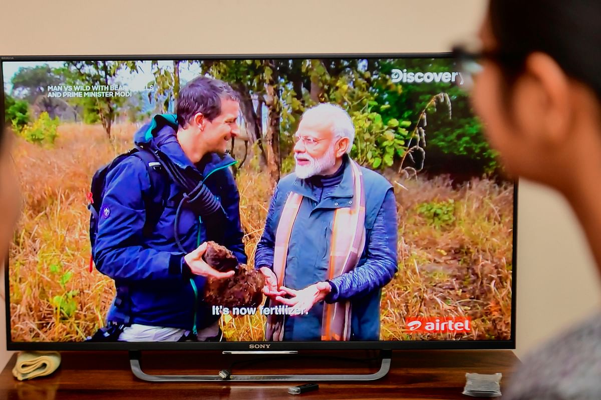 People watch on television the special edition of `Man Vs Wild` series hosted by survival expert Bear Grylls (R), going on a mission with Indian prime minister Narendra Modi, in Bangalore on 12 August. Photo: AFP