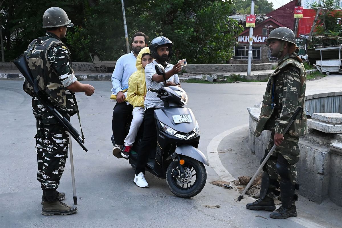 A motorist shows his identity card to a security personnel after being stopped for questioning at a roadblock during a lockdown in Srinagar on 12 August 2019. Photo: AFP