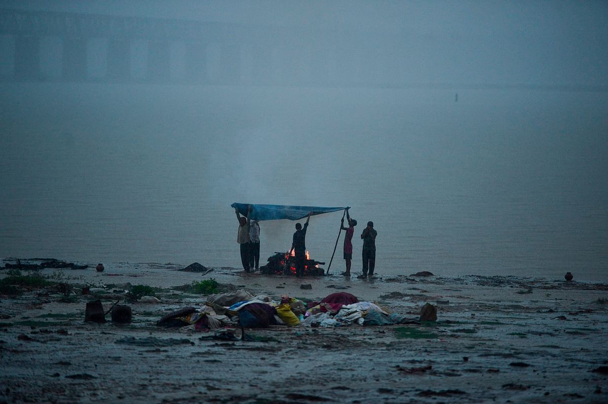 Mourners protect with a plastic sheet a burning body as they perform a cremation during heavy rains on the bank of the Ganges river in Allahabad on 13 August 2019. Photo: AFP