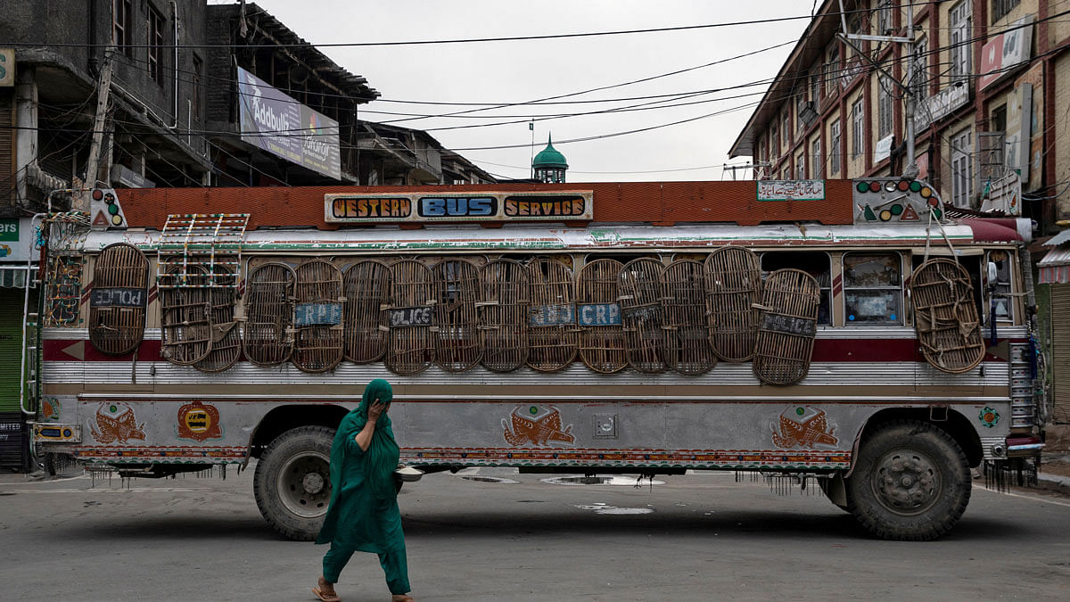 A Kashmiri woman walks past a bus used as a road block by Indian security personnel during restrictions after the scrapping of the special constitutional status for Kashmir by the government, in Srinagar, on 11 August 2019. Reuters File Photo