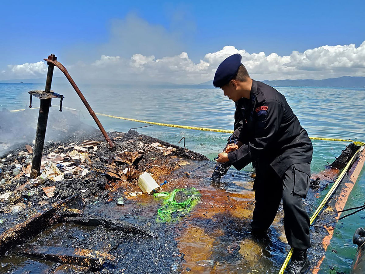 This handout picture taken on 17 August, 2019 and released by Kendari police shows an Indonesian policeman inspecting the charred remains of a ferry that caught fire near Kendari, off Indonesia`s Sulawesi island. Photo: AFP