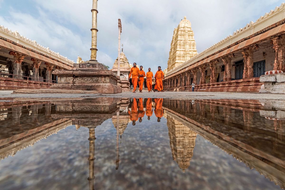 Members of Virupaksha Temple and Hindu devotees walk in the temple`s premises, as their reflections are seen in a puddle of water in Hampi on 17 August 2019. Photo: AFP