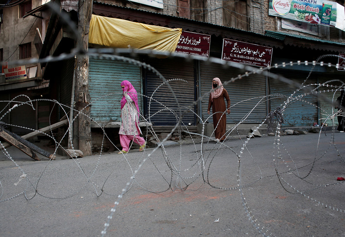 Kashmiri women walk past concertina wire laid across a road during restrictions after the scrapping of the special constitutional status for Kashmir by the Indian government, in Srinagar, on 20 August 2019. Photo: Reuters