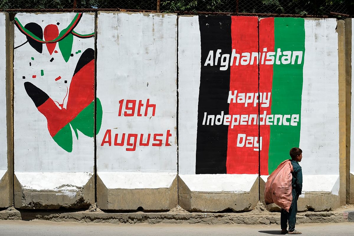 A boy collecting useable items from streets walks past a mural on a security barrier wall as the country celebrates its 100th anniversary of Independence Day in Kabul on 19 August 2019. Photo: AFP