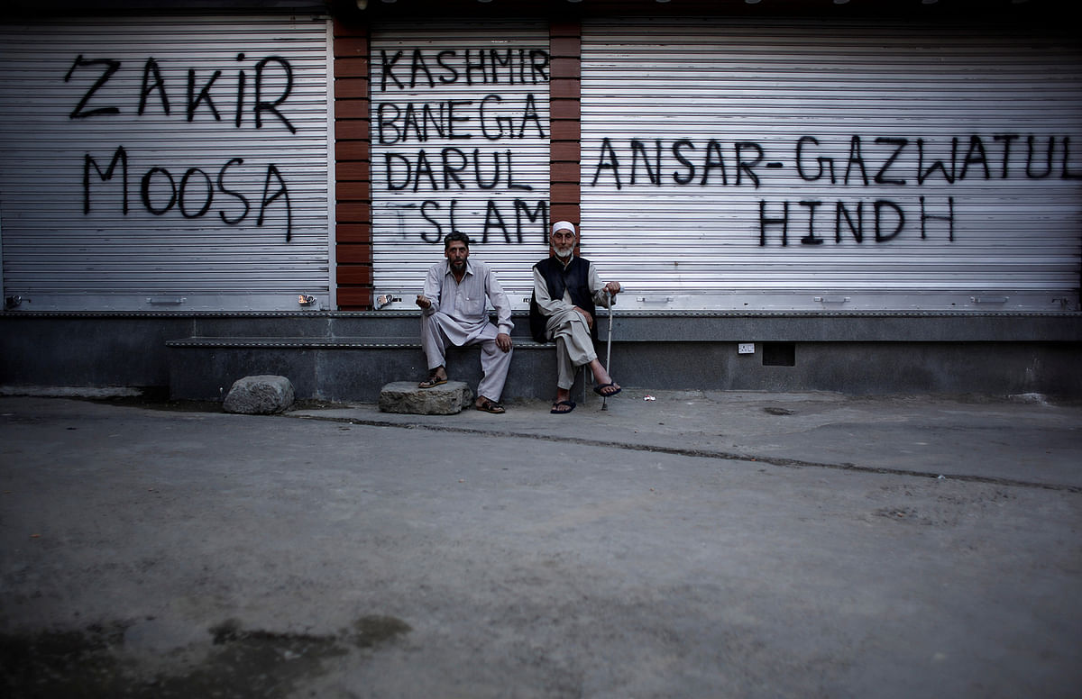 Kashmiri men sit in front of the closed shops painted with graffiti during restrictions after scrapping of the special constitutional status for Kashmir by the Indian government, in Srinagar, on 20 August 2019. Photo: Reuters