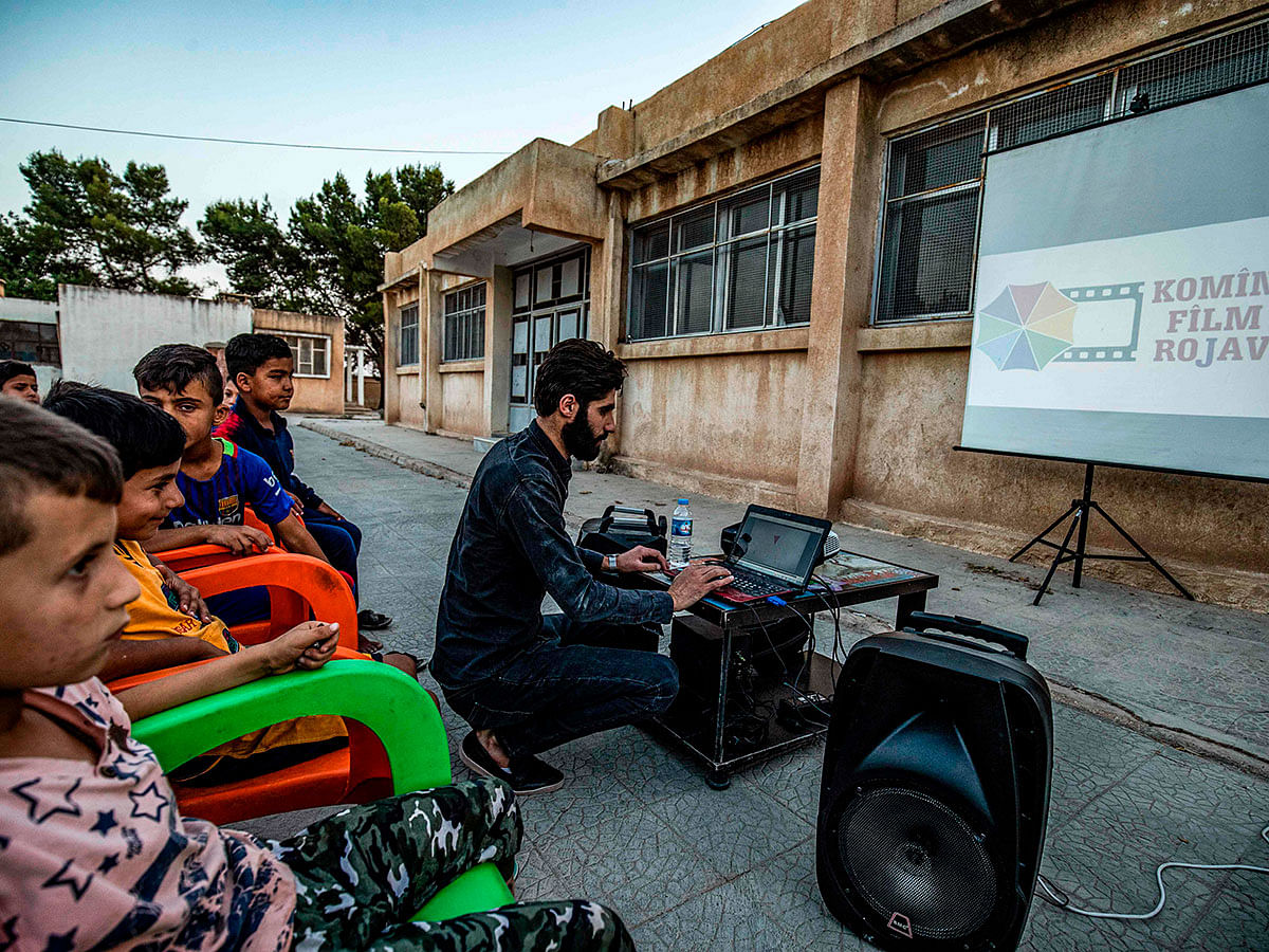 A member of Syrian-Kurdish filmmaker Shero Hinde`s mobile cinema `Komina Film` initiative prepares a laptop connected to a projector and screen for a film screening for children at a school yard in the village of Shaghir Bazar, 55 kilometres southeast of Qamishli in the Kurdish-populated areas of north-eastern Syria`s Hasakeh province, on 28 July, 2019. Photo: AFP
