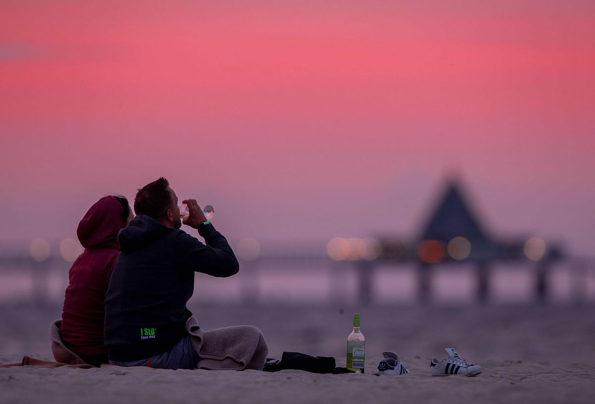 A man and a woman have a glass of wine as setting sun paints the sky in shades of red at the Baltic Sea beach of Ahlbeck on the island of Usedom, northeastern Germany, on 20 August 2019. Photo: AFP