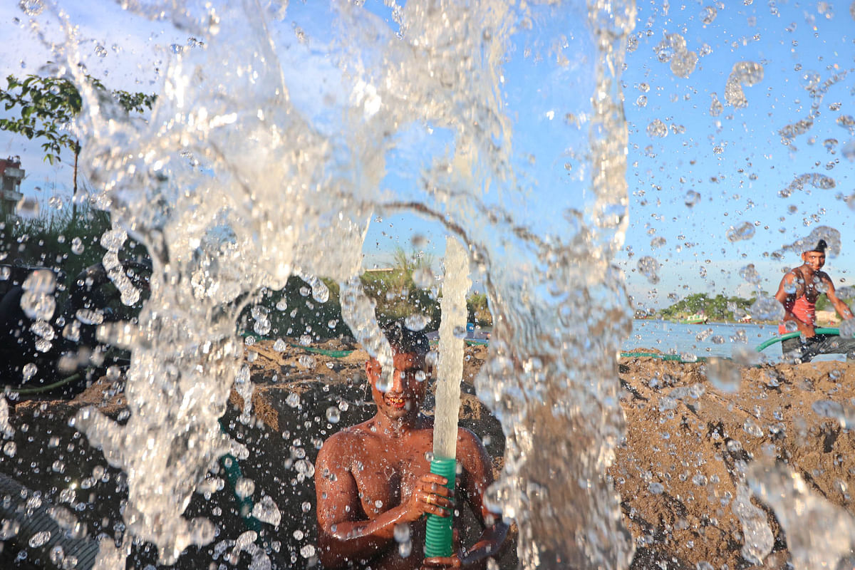 A worker bathes while hosing down sand loaded on a boat during a hot day at Badaghat, Sylhet on 26 August 2019. Photo: Anis Mahmud