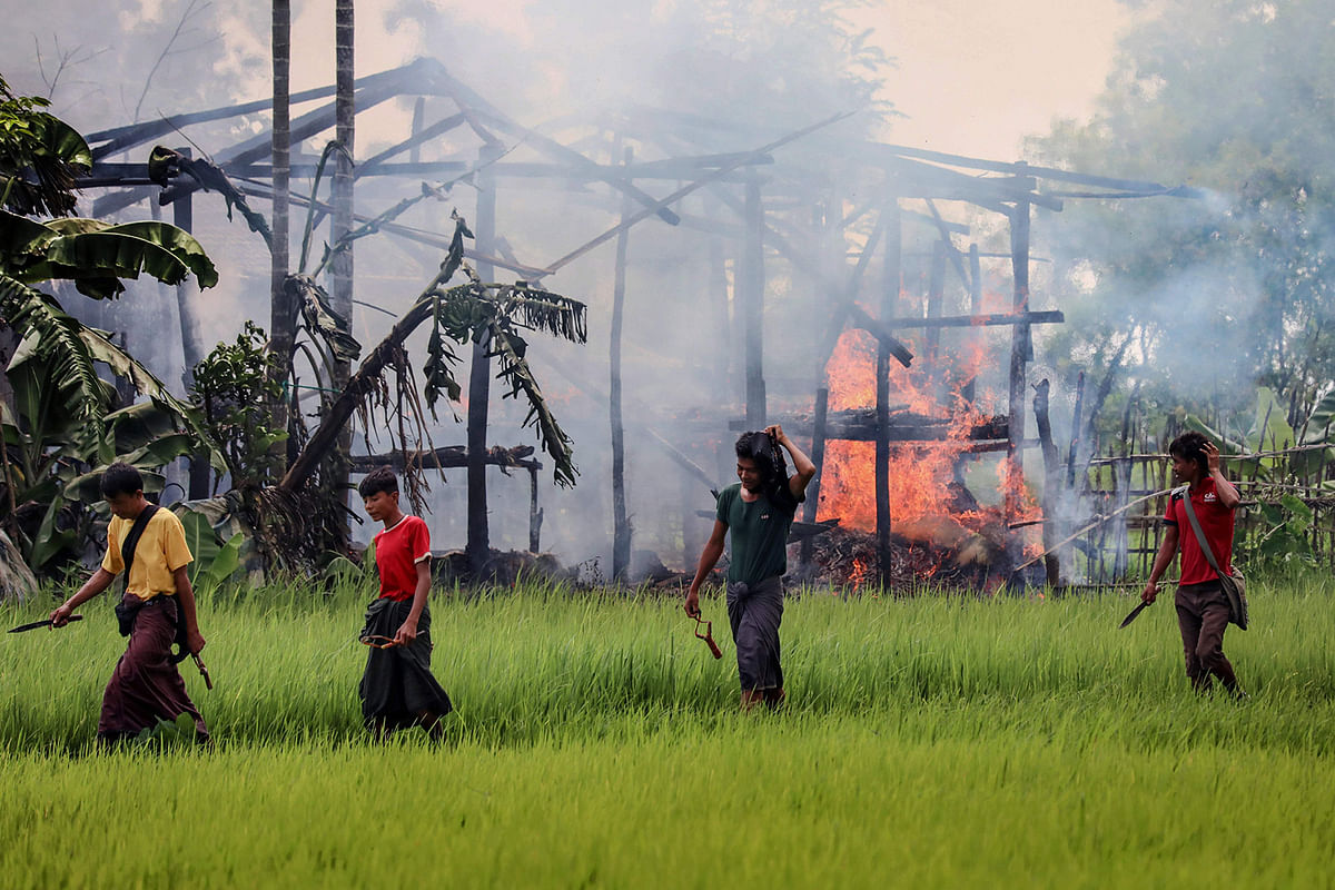 In this file photo taken on 7 September 2017 unidentified men carry knives and slingshots as they walk past a burning house in Gawdu Tharya village near Maungdaw in Rakhine state in northern Myanmar. Photo: AFP
