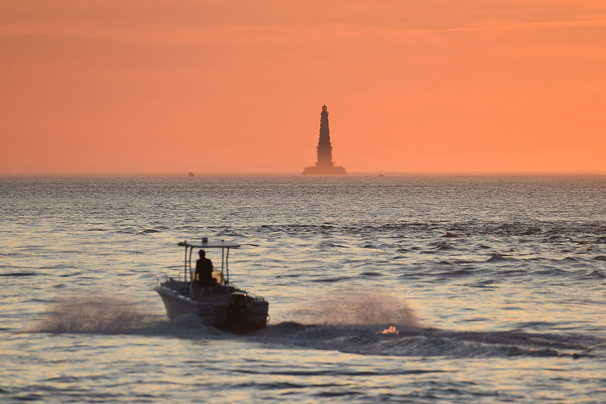A boat sails at sunset on 23 August 2019 off the coast of Le Verdon-sur-Mer, southwestern France, with the Cordouan lighthouse in the background. Photo: AFP