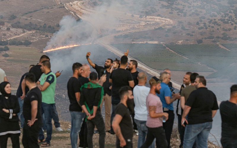 People flash the victory gesture as they pose for a “selfie” photo on a cell phone while others watch as fires blaze along the Lebanese side of the border with Israel in the Lebanese village of Maroun al-Ras on 1 September following an exchange of fire between the Shiite Muslim Lebanese movement Hezbollah and Israel. Photo: AFP