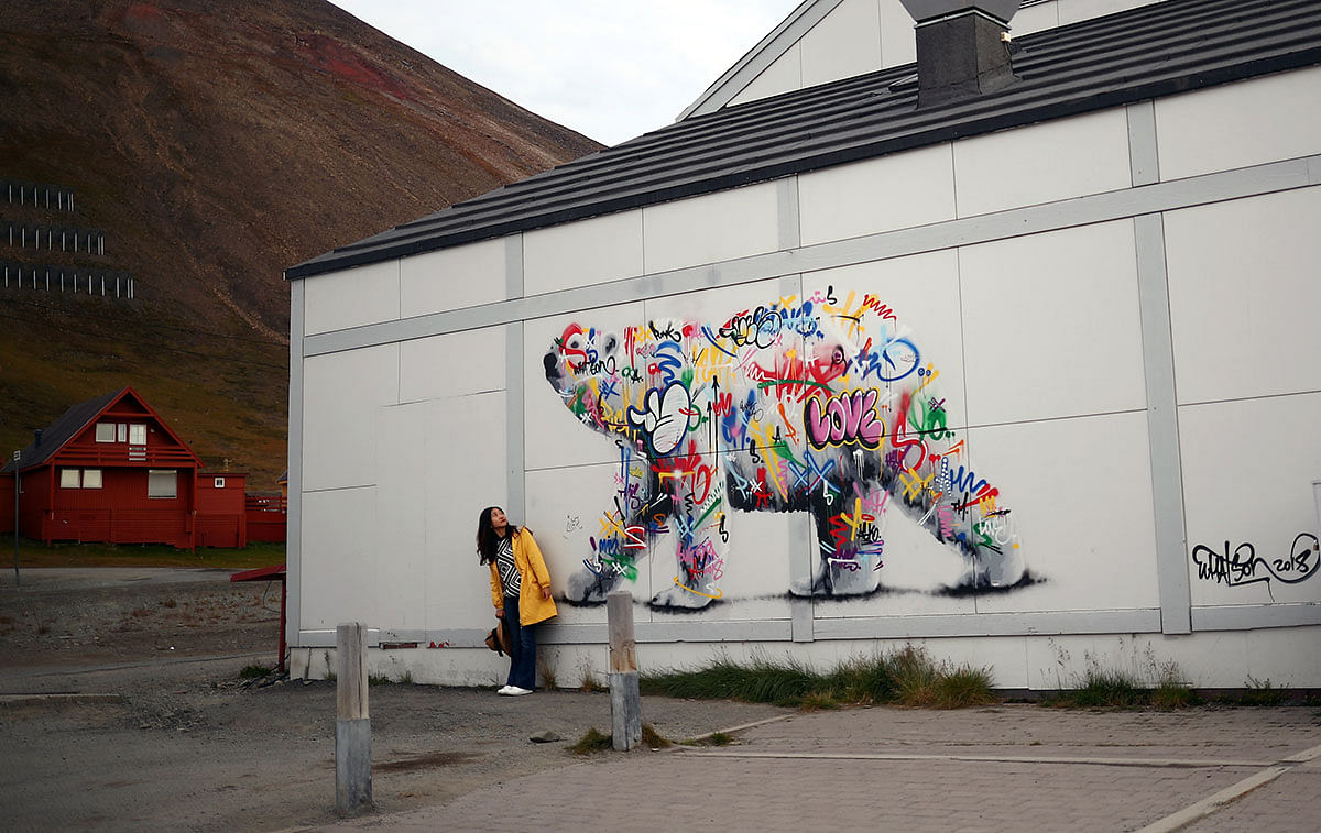 A woman poses next to a polar bear mural in the town of Longyearbyen in Svalbard, Norway, 6 August 2019. Photo: Reuters