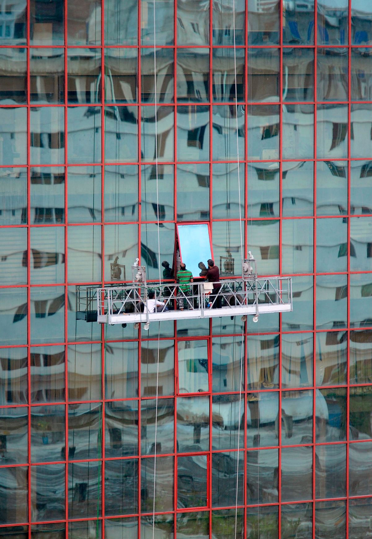 Bangladeshi workers fix a glass window onto a high rise building in Dhaka on 4 September 2019. Photo: AFP