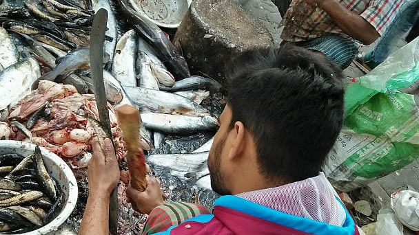 A man uses a piece of wood and knife to remove the scales of a fish at Panthapath Tejgaon Link Road, Dhaka on 27 August 2019. Photo: Nusrat Nowrin