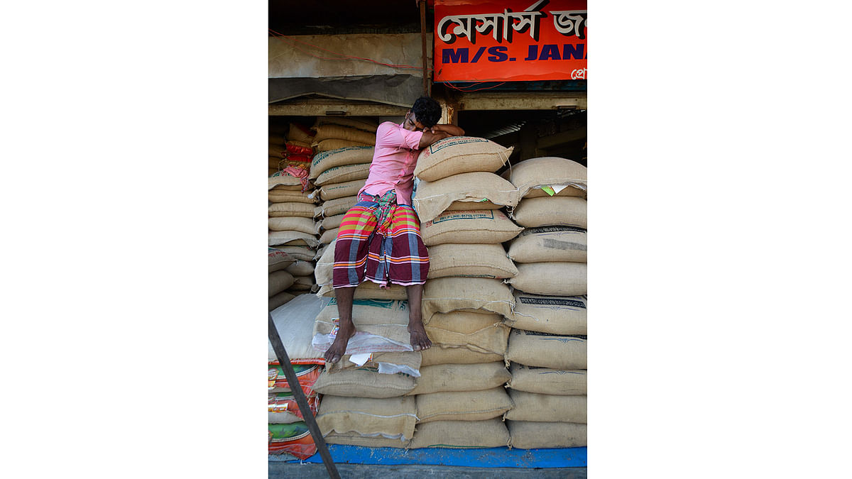 A vendor sleeps on rice sacks at his shop in Kawran Bazar wholesale market in Dhaka on 8 September, 2019. Photo: AFP