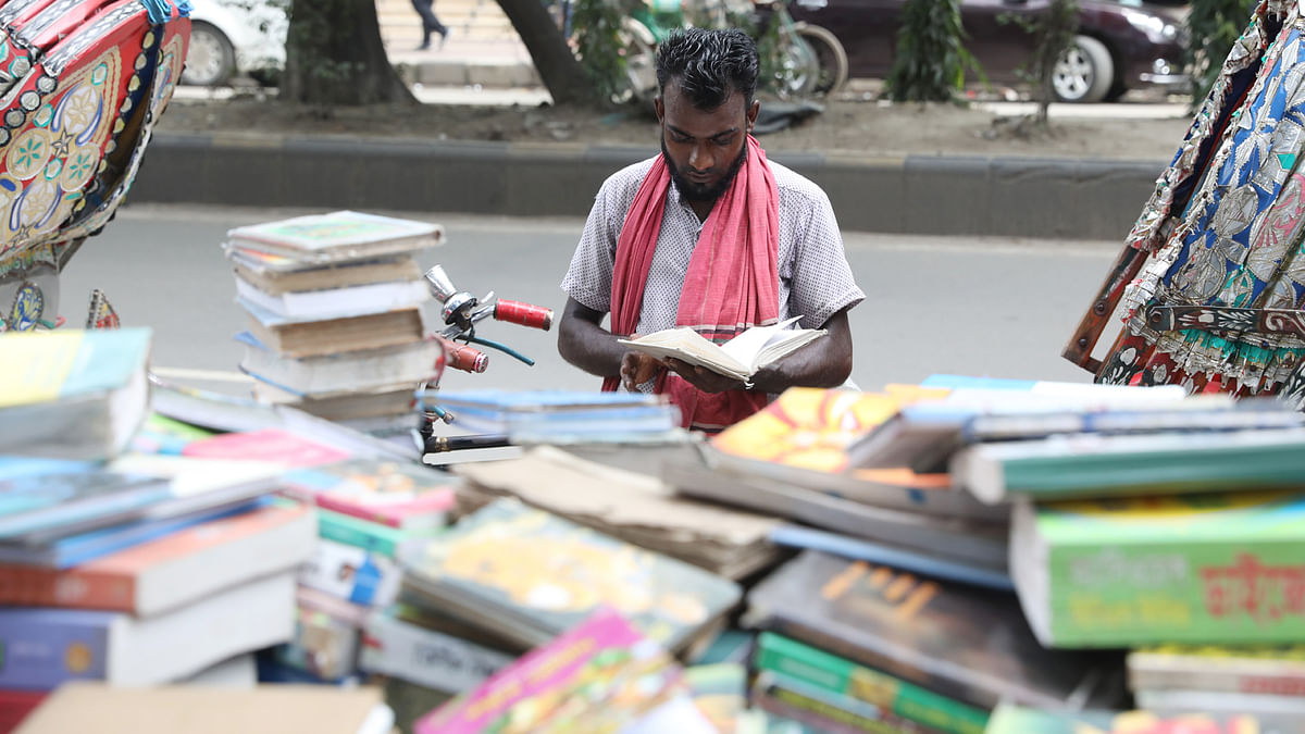 A rickshaw puller reads a book in front of a street book shop at Bijoynagar in Dhaka, 10 September 2019. Photo: Abdus Salam