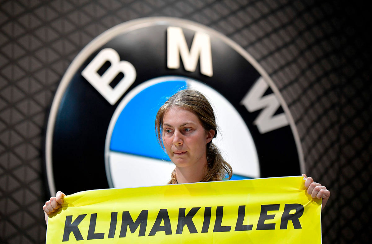 A Greenpeace activist standing on a BMW car holds a poster reading `Climate Killers` as she demonstrates at the booth of German car maker BMW, where German Chancellor Angela Merkel touring the fair grounds was expected after officially opening the International Auto Show (IAA) in Frankfurt am Main, western Germany, on 12 September 2019. Photo: AFP