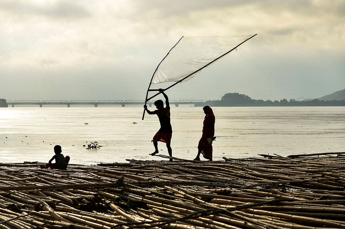 A man fishes along with his family as they stand on floating bamboo logs in the Brahamaputra river in Guwahati in the northeastern state of Assam on 14 September 2019. Photo: AFP