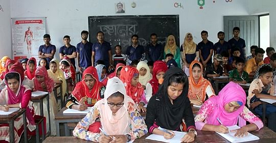 Students of ‘Gyaner Pathshala’ answer questions in a test while the teachers pose for the camerabehind them. Photo: Prothom Alo