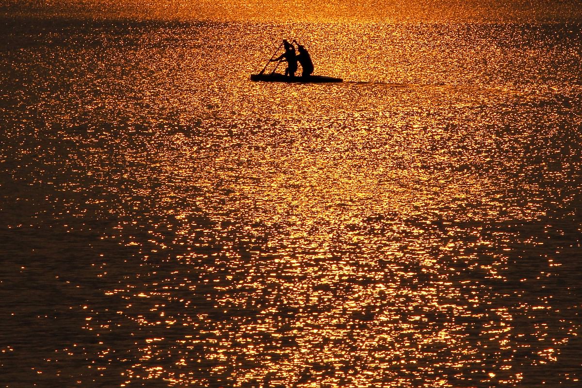 Row-men with their boat are silhouetted in the waters of Sukhna Lake during sunrise in Chandigarh on 22 September 2019. Photo: AFP
