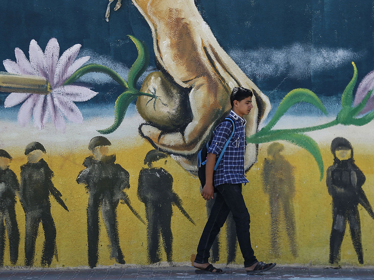 A Palestinian student walks past a mural along a street in Rafah, in the southern Gaza Strip, on 25 September 2019. Photo: AFP