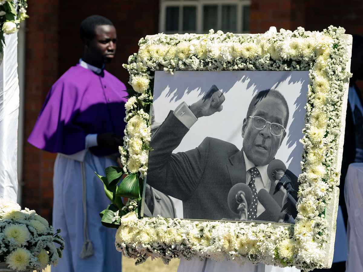 A priest walks past a portrait of Robert Mugabe during the burial of the former Zimbabwe leader at his home village in Kutama, on 28 September, 2019. Photo: AFP