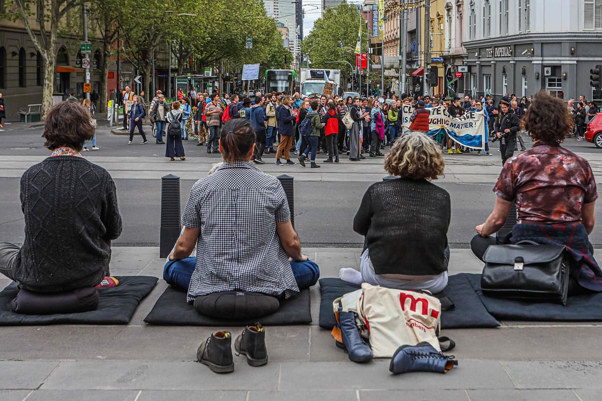 Protesters (in background) block a city intersection outside the Victoria state parliament as another group (bottom) meditate to mark the beginning of the Extinction Rebellion protests in Melbourne on 7 October 2019. Photo: AFP
