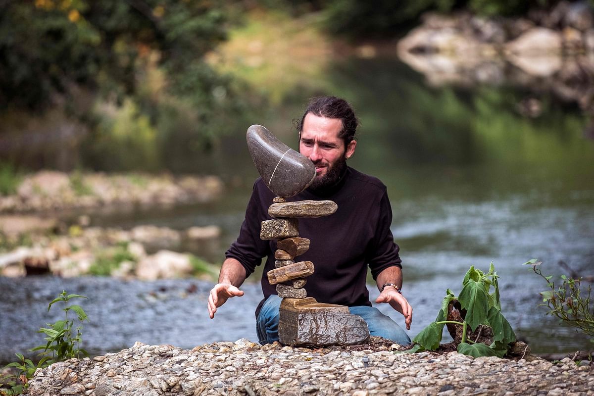 French artist and rock balancer SP Ranza looks at his temporary sculpture made of stones collected in the river on 10 October 2019 near Mazamet, southern France. Photo: AFP