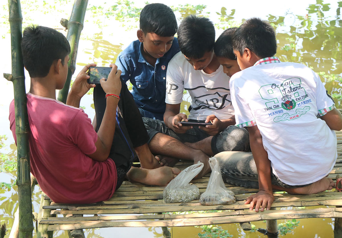 A group of teens playing in mobile near a pond in Aria of Shahjahanpur upazila of Bogura on 14 October 2019. Photo: Soel Rana