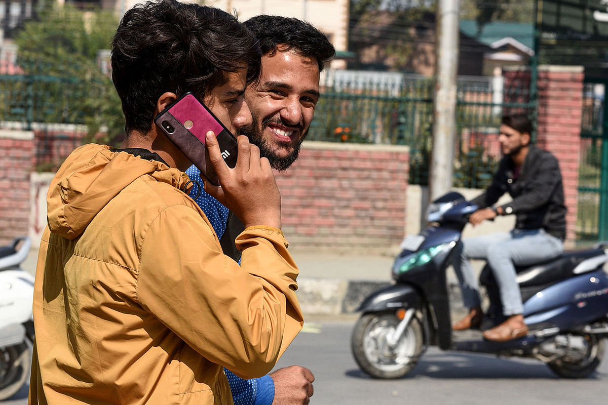 A youth looks on as another one speaks on a mobile phone in Srinagar on 14 October 2019, following Indian government`s decision to restore mobile phones network in Indian-administered Kashmir. Photo: AFP