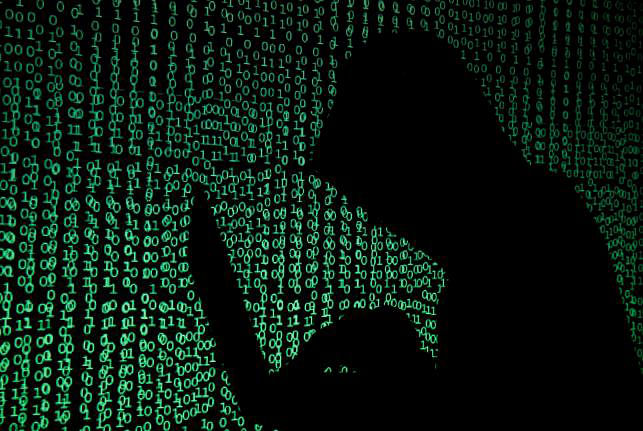 Hooded man holds laptop computer as cyber code is projected on him in this Reuters` illustration.