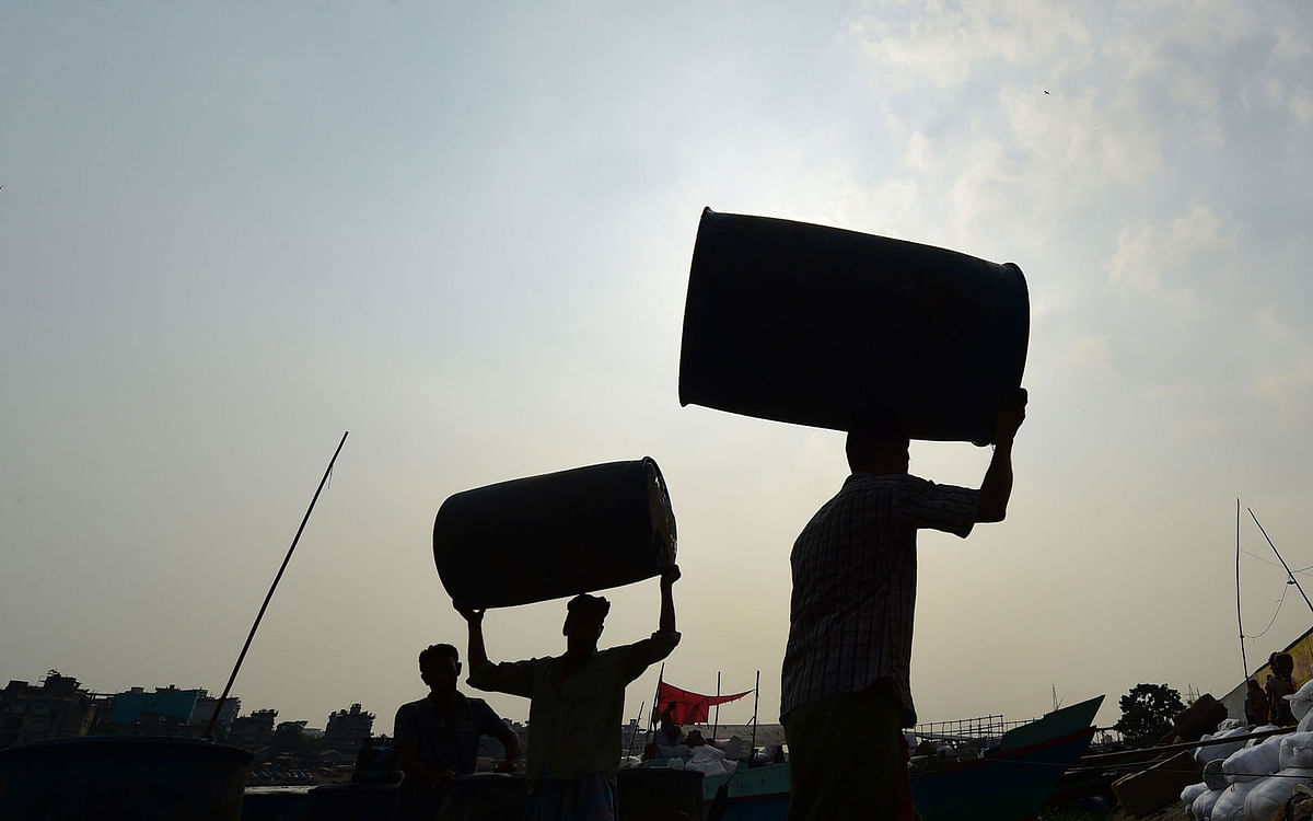 Workers unload used barrel drums in Buriganga river in Dhaka on 15 October 2019. Photo: AFP