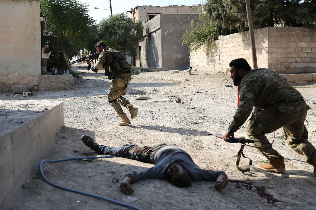 Turkish-backed Syrian fighters take cover next to corpses in the Syrian border town of Ras al-Ain on 17 October during Ankara`s deadly offensive against Kurdish forces. Photo: AFP